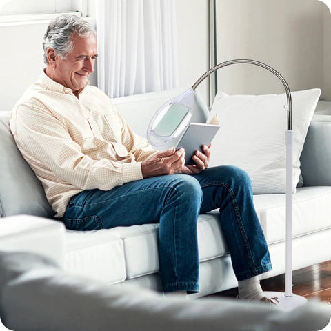 Man using LightView Pro LED Magnifying Floor Lamp with Full Page Glass Lens, Daylight Full Spectrum Light, reading on a sofa.