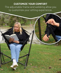 Person sitting in Portable Hammock Camping Chair With Stand by a lake, showing adjustable straps, suitable for outdoor use