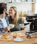 Couple enjoying coffee with the Pro Espresso Maker With Auto Milk Frother on the table next to pastries and latte art.