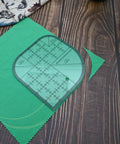 Clear Acrylic Quilting Ruler With Templates And Curved Corner Cutter For Precise Fabric Cutting placed on green fabric.