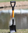 Medium Square Shovel With D Cup Handle 27 Inch Length Durable Build Comfortable Grip For Gardening Landscaping Snow Removal And Light Construction Tools 1 Pack Workhorse Shovel standing upright on grass by water.