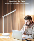 Dimmable Desk Lamp With USB Charging Ports, 10 Brightness Levels And 5 Color Temperature beside a man reading on a laptop.