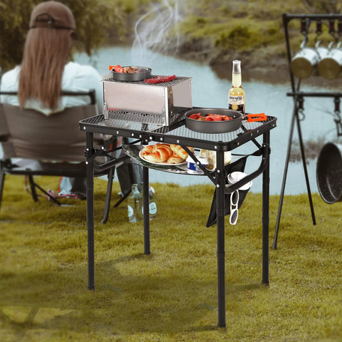 Small Folding Grill Table For Outdoors With Three Adjustable Heights Lightweight Portable Aluminum Camp Table For Camping Picnics BBQ Black 24 By 16 Inches set up by a river.