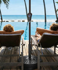 Beefed Up Heavy Duty Outdoor Umbrella Base For Market Umbrellas, 81.5 Lb Capacity Water Filled Base by poolside with loungers.