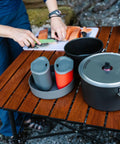 Ultralight Two Person Backpacking Camping Cook Set With 1.5L And 2.5L Hard Anodized Nonstick Pots Strainer Lid And Two Deep Dish Plates For Backcountry Meals displayed on a wooden table.