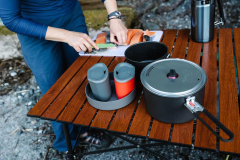 Ultralight Two Person Backpacking Camping Cook Set With 1.5L And 2.5L Hard Anodized Nonstick Pots Strainer Lid And Two Deep Dish Plates For Backcountry Meals displayed on a wooden table.