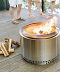 Juniper Aromatic Firewood for Outdoor Fire Pits and Backyard Fires Kiln Dried Logs beside a lit stainless steel fire pit