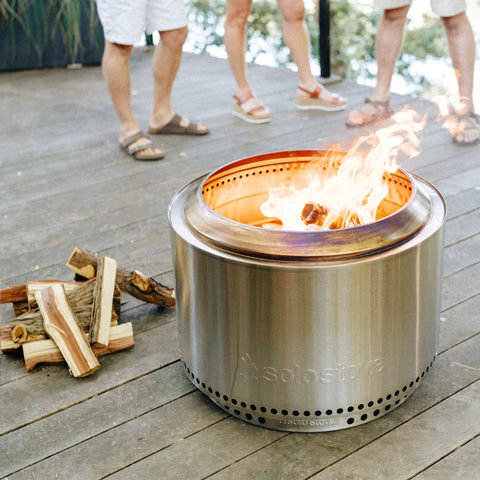 Juniper Aromatic Firewood for Outdoor Fire Pits and Backyard Fires Kiln Dried Logs beside a lit stainless steel fire pit