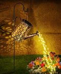 Solar Watering Can With Lights For Outdoor Garden Decor with 90 LEDs shining over flowers, hanging on shepherd hook.