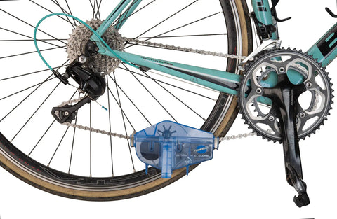 Cyclone Chain Scrubber CM-5.3 in blue attached to a multi-speed bike, showing chain cleaning process with easy grip handle.
