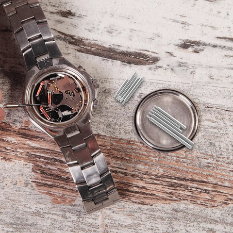 Watch Band Pins Replacement Kit For Metal Watch Straps With Spring Bars next to open watch back on wood surface