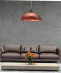 Red industrial-style pendant light hanging over a brown sofa with flowers on the coffee table, featuring rough textured walls.