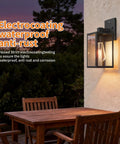 Dusk To Dawn Outdoor Wall Light With Automatic Sensor Solid Black Metal Coach Lantern Waterproof Porch Fixture mounted on wall beside wooden table.