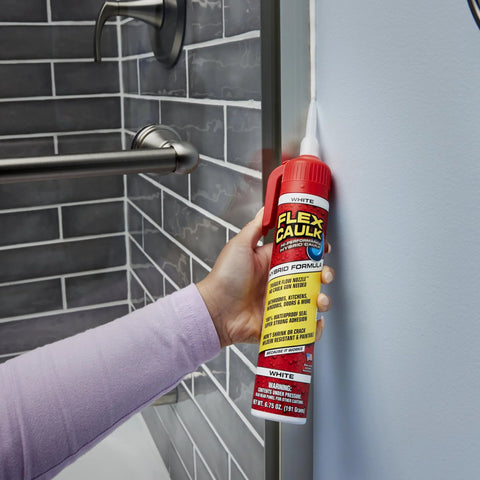 Flex Caulk white 9 oz sealant tube held in hand near a glass shower door for sealing joints