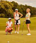 Three women on a golf course putting green, showing expressions of surprise and excitement while playing golf.