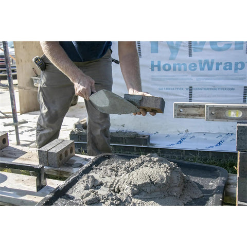 Worker using London Style Brick Trowel With DuraSoft Handle For Brickwork Blockwork And Stonework High Carbon Steel One Piece Forged Pro Grade Blade With Polished Finish Made In USA Size Ten By Four And Five Eighths Inch Masonry Tool to apply mortar to bricks