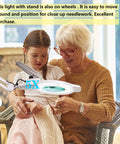 Ultra Bright 5X Magnifying Floor Lamp With Rolling Base, used by elderly woman and child for detailed needlework, white