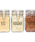 Three glass jars filled with rice, buckwheat, and oatflakes, labeled in black lettering, used for organizing kitchen ingredients.