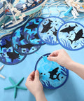 24 Pack Summer Shark Crafts Kit With Tissue Paper Suncatchers, hands assembling blue shark decoration on table