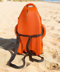 Spearfishing Float Buoy With Foldable Carbon Fiber Flagpole on sandy beach, orange red, with attached straps visible.