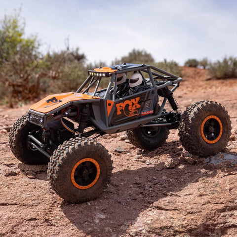 Capra UTB18 One Eighteenth Scale RC Crawler 4WD RTR on rocky terrain, showing tube chassis and four-link suspension in multicolor gray.