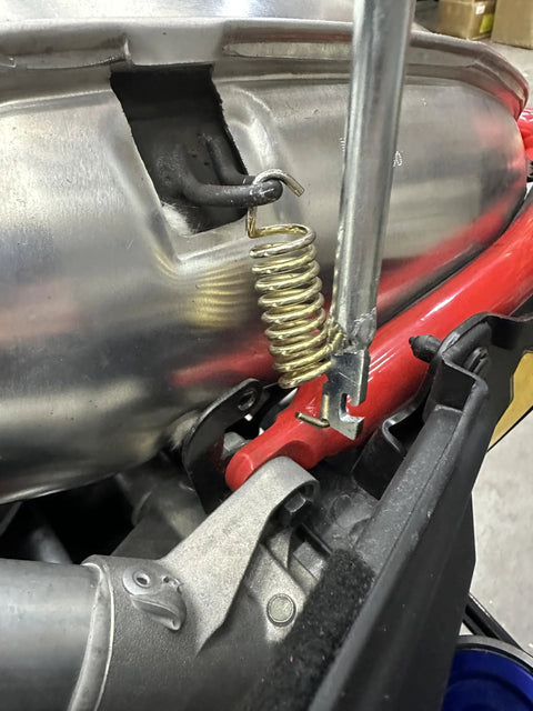 Exhaust spring removal tool installed on snowmobile exhaust; 19-inch metal tool with coil spring and red bracket.