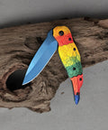 Colorful Parrot Pattern Folding Pocket Knife With Gradient Parrot-Scale Handle, 3-Inch Blue Coated Blade on wood surface.