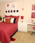 Bedroom with modern decor featuring red bedspread, wall art, and decorations. Desk in corner with office items visible.