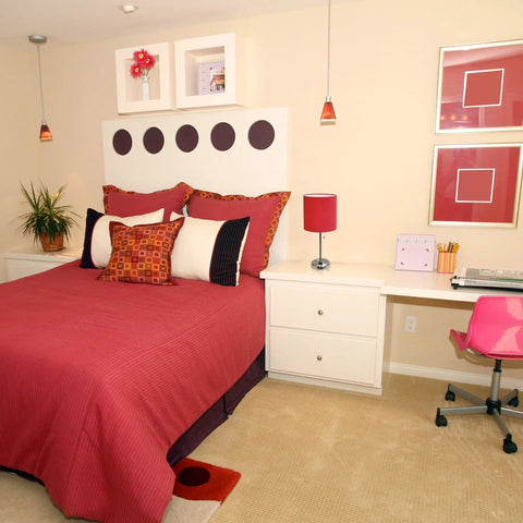 Bedroom with modern decor featuring red bedspread, wall art, and decorations. Desk in corner with office items visible.