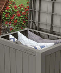 Open 22 Gallon Outdoor Storage Box With Seat In Stone Gray Resin, showing interior with cushions, in garden setting.
