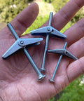 Hand holding three toggle bolts from Toggle Bolt Kit 29-Piece Zinc Plated Steel Set With One-Eighth Inch, Three-Sixteenth Inch, And One-Fourth Inch Toggle Bolts Plus Wing Nuts For Hanging Heavy Stuff On Drywall.