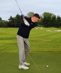 Golfer using Pro Grade Golf Swing Trainer Plate With 2 Premium Gold Alignment Rods, Swing Analyzer Aid on green field