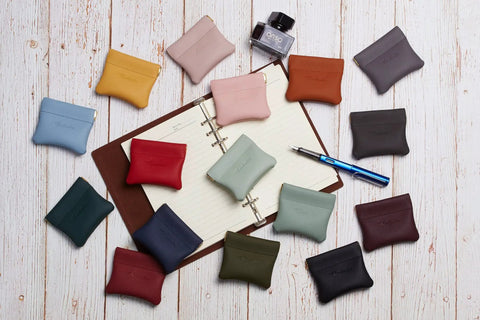 Smooth Vintage Black Leather Squeeze Coin Purse With Heavy Duty Spring Frame, Super Compact Change Holder And Cash Pocket For Hassle Free Everyday Carry By Men And Women on wood background with various colors.