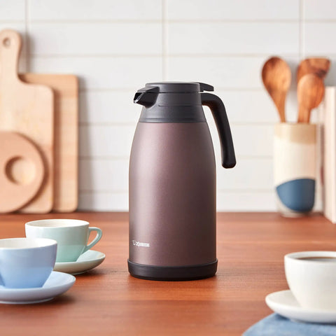 Stainless Steel Vacuum Carafe 1.9 L With One-Touch Pour, Tank-Grade Build For Serious Heat Retention, Unbreakable Steel, 2.5 Inch Wide Opening, Screw-Off Lid, Keeps Coffee Hot Or Cold, Brown on kitchen countertop.