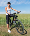 Person standing with a mountain bike in a field, showcasing inflated tires using 2-Pack 26 Inch Bike Tubes 26x1.50/1.75 With 32mm Schrader Valve Inner Tubes Compatible With 26x1.50/1.75 Tires Premium Butyl Rubber For Tight Seal And Easy Install On Road And Mountain Bikes.