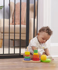 Child plays near Extra Wide Baby Gate For Doorways And Stairs, 30 To 41.5 Inches, Pressure Mounted Wood Gate With Door, One Hand Open.