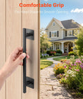Rustic Barn Door Handle 12.6 Inch Built Tough for All Weather Gates Heavy Duty Carbon Steel Pull With Rust Resistant Coating Easy Install Sliding Door Handle for Garage Shed Closet Pantry Black Finish shown on a wooden door with a hand gripping it, garden and house visible in background.
