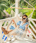 Woman relaxing in Caribbean Hammock Chair with 40-Inch Hardwood Spreader Bar and Soft-Spun Cotton Rope on a balcony.