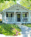 House with address number 207 above the front porch, surrounded by greenery and colorful flowers in springtime.