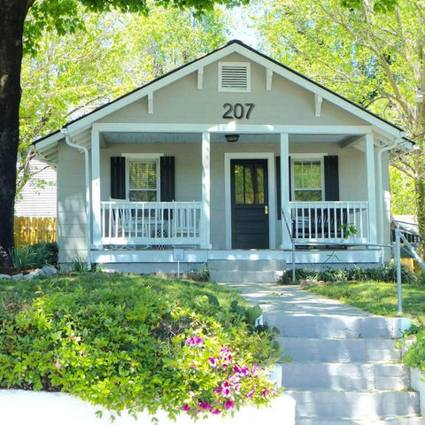 House with address number 207 above the front porch, surrounded by greenery and colorful flowers in springtime.