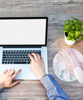 Person using laptop beside Pink Marble Round Mouse Pad With Premium Textured Surface, Washable And Non Slip Rubber Base, 7.87 By 7.87 Inches, 3 mm Thick Desktop Protector For Work And Gaming, Durable Stitched Edges, Customizable Design.
