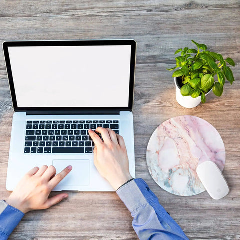 Person using laptop beside Pink Marble Round Mouse Pad With Premium Textured Surface, Washable And Non Slip Rubber Base, 7.87 By 7.87 Inches, 3 mm Thick Desktop Protector For Work And Gaming, Durable Stitched Edges, Customizable Design.