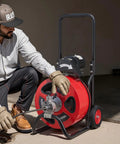 Man using Full Throttle Auto Feed Sewer Snake Auger 100 Ft Steel Cable to clear a drain blockage with gloves.