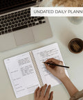 Daily Planner With Hourly Schedule Spiral Notepad For Easy Tasking And Appointment Organization on desk beside laptop and paperclips.