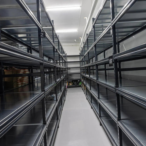 Empty black metal shelving units in a warehouse aisle with overhead lighting.