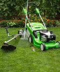 Green lawn mower and weed trimmer on lush grass with garden tools and flowers in background.