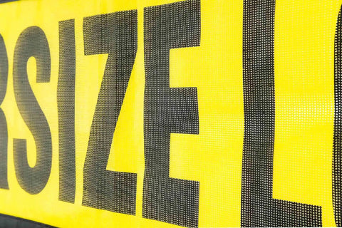 Close-up of Two Pack 18x84 Oversize Load Sign for Trucks with Bungee Cord and Hook, Stretch Cord Mesh Banner, part of warning text visible.
