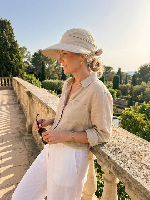 Woman outdoors wearing 2-In-1 Women's Sun Visor Hat With Wide Brim Or Zip-Off Top, UPF 50+ Sun Protection, holding sunglasses.