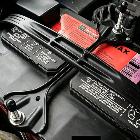 Badass 18-8 Stainless Steel J Hook Battery Hold Down Bolts Kit securing a car battery with black retention strap and bolts.