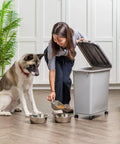Woman using Portable 40Lb Pet Food Storage Bin With Wheels, Airtight Lid, Built In Scoop In Lid, BPA Free, Durable Gray Dog Food Organizer